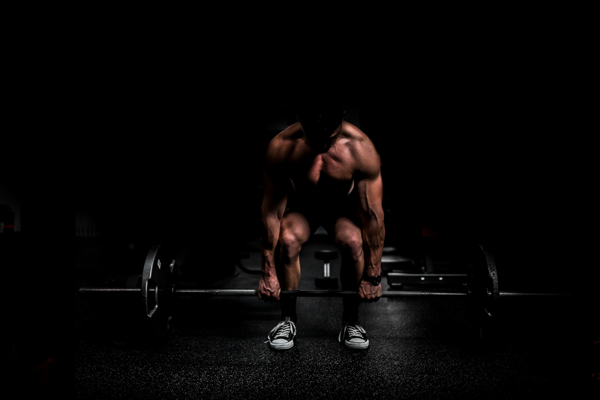 A lifter crouched over a loaded barbell in a dark gym